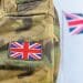 Close up of a soldier's arm in camo with a union flag badge. A union flag is flying in the background. Defence Universities Alliance