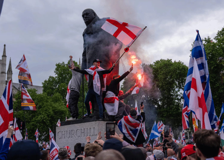 People, largely white men, sit on a Winston Churchill statue with flares and wearing Union Jack, England and Scotland flags as they take part in the rally where Muslims experienced hate speech