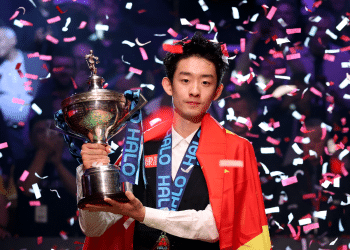 Wu Yize holds his 2026 World Snooker Championship trophy while confetti falls around him. Yize has the China flag draped over his suit.