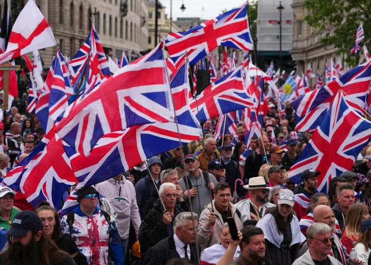 LONDON, ENGLAND - MAY 16: People take part in a Unite The Kingdom far right protest on May 16, 2026 in London, England. The far-right "Unite the Kingdom" rally, organised by Tommy Robinson is expected to draw a crowd of 50,000. Under strict Public Order Act conditions, demonstrators are legally confined to a specific south-bound corridor from Kingsway to Parliament Square between late morning and early evening. To prevent clashes with a concurrent 30,000-strong counter-protest, the Metropolitan Police has launched an unprecedented £4.5 million security operation deploying over 4,000 officers. The operation is using live facial recognition, armoured vehicles, and stringent hate speech monitoring, while the Home Office has barred multiple international far-right speakers from entering the UK. (Photo by Carl Court/Getty Images)