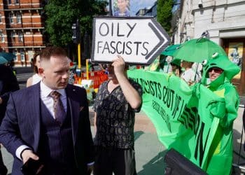 A suited man walks past protesters outside the ARC conference in London. A sign says Oily Fascists