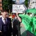 A suited man walks past protesters outside the ARC conference in London. A sign says Oily Fascists