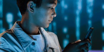 Social media: Side view of teenage boy using phone against a digital tech backdrop