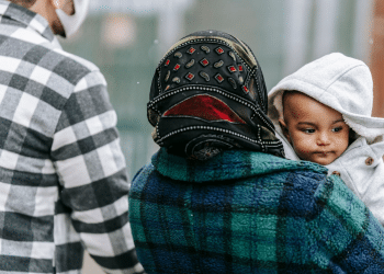 Asylum seeker story: A couple walking outside and the woman is holding a toddler. Only his face is visible.