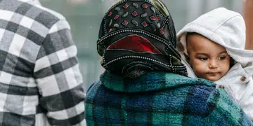 Asylum seeker story: A couple walking outside and the woman is holding a toddler. Only his face is visible.