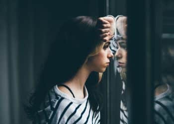 Stock image of girl looking through window, illustrating mental health outcomes
