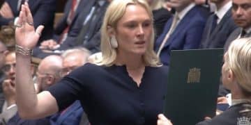 Lara Bird with her right hand in the air in Parliament and her three middle fingers appear to be crossed