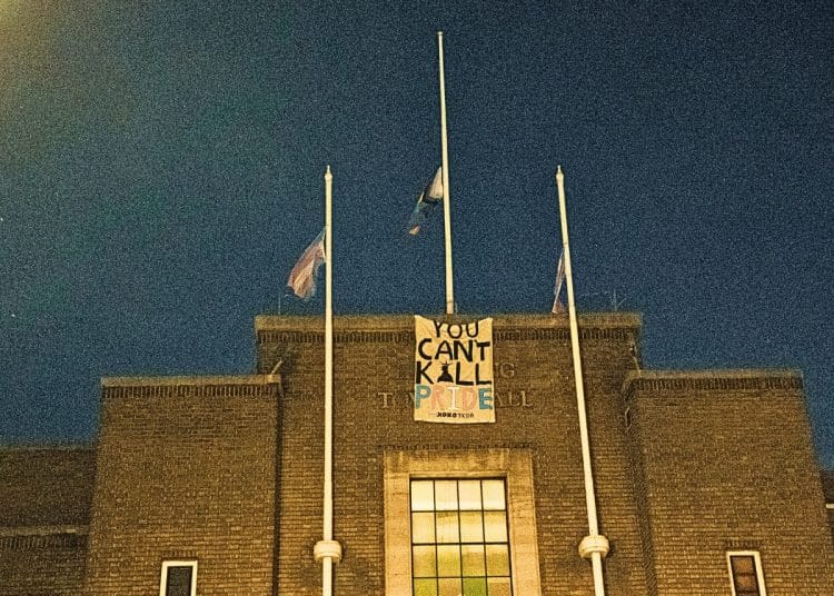 Havering Town Hall with Pride and Trans flags flying from flagpoles and a banner saying YOU CAN’T KILL PRIDE - XOXO TKDB