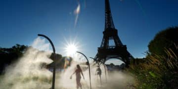 People walk under cooling sprays in front of the Eiffel Tower during a heatwave in Paris