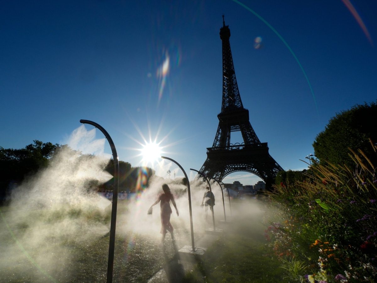 People walk under cooling sprays in front of the Eiffel Tower during a heatwave in Paris