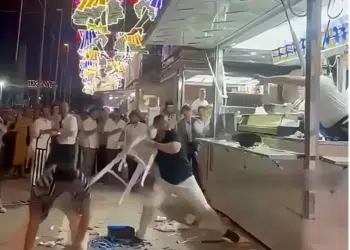 A screenshot of the video showing a pair of Israeli men, allegedly intoxicated, with one holding a plastic stool in his hand about to launch it at the stall and its three staff members
