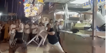 A screenshot of the video showing a pair of Israeli men, allegedly intoxicated, with one holding a plastic stool in his hand about to launch it at the stall and its three staff members