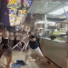 A screenshot of the video showing a pair of Israeli men, allegedly intoxicated, with one holding a plastic stool in his hand about to launch it at the stall and its three staff members