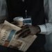 The torso of a male journalist holding a copy of the Financial Times, with a cardboard cup holding a drink, and you can see a press card attached to a lanyard around his neck. His neck upwards is not visible