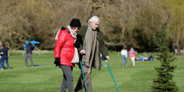 Carers Week: An older pair, one with two crutches, and the other locking their arm, walk and enjoy the spring sunshine at Mottisfont one of the National Trust parklands on 21 March 2020 in Romsey, UK