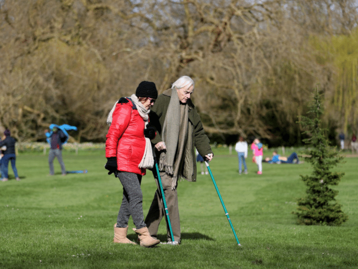 Carers Week: An older pair, one with two crutches, and the other locking their arm, walk and enjoy the spring sunshine at Mottisfont one of the National Trust parklands on 21 March 2020 in Romsey, UK