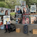 Posters with 'Free XYZ' line a wall and one woman holds one saying 'Free Rowan Gibson'. They are part of the protestors jailed for demonstrating outside an ICE centre