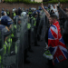 Armed riot police hold their shields up in a row while men, one at the front with Union Jack flag draped on his back, show Nazi salutes. Skwawkbox argues Israel-bought politicians show hypocrisy when responding to riots and protests