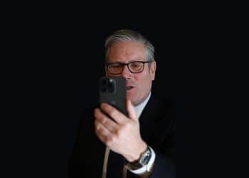 Keir Starmer looking at a phone against a dark background Social media