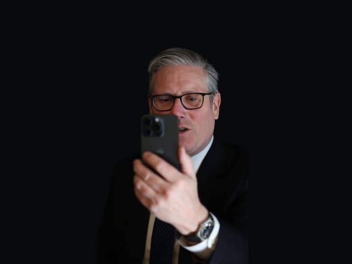Keir Starmer looking at a phone against a dark background Social media
