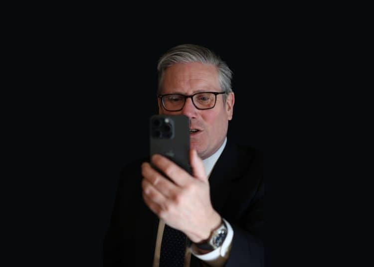 Keir Starmer looking at a phone against a dark background Social media