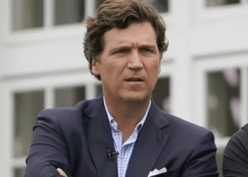 Tuckder Carlson wearing a suit with the top button of his shirt undone and his arms crossed at the final round of the Bedminster Invitational LIV Golf tournament in Bedminster, New Jersey, in the US, on 31 July 2022