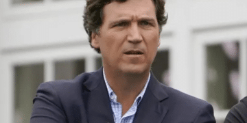 Tuckder Carlson wearing a suit with the top button of his shirt undone and his arms crossed at the final round of the Bedminster Invitational LIV Golf tournament in Bedminster, New Jersey, in the US, on 31 July 2022