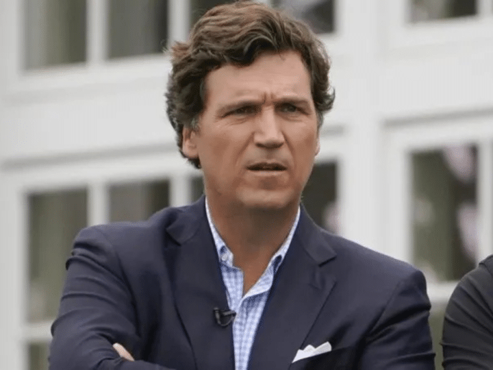 Tuckder Carlson wearing a suit with the top button of his shirt undone and his arms crossed at the final round of the Bedminster Invitational LIV Golf tournament in Bedminster, New Jersey, in the US, on 31 July 2022