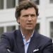 Tuckder Carlson wearing a suit with the top button of his shirt undone and his arms crossed at the final round of the Bedminster Invitational LIV Golf tournament in Bedminster, New Jersey, in the US, on 31 July 2022