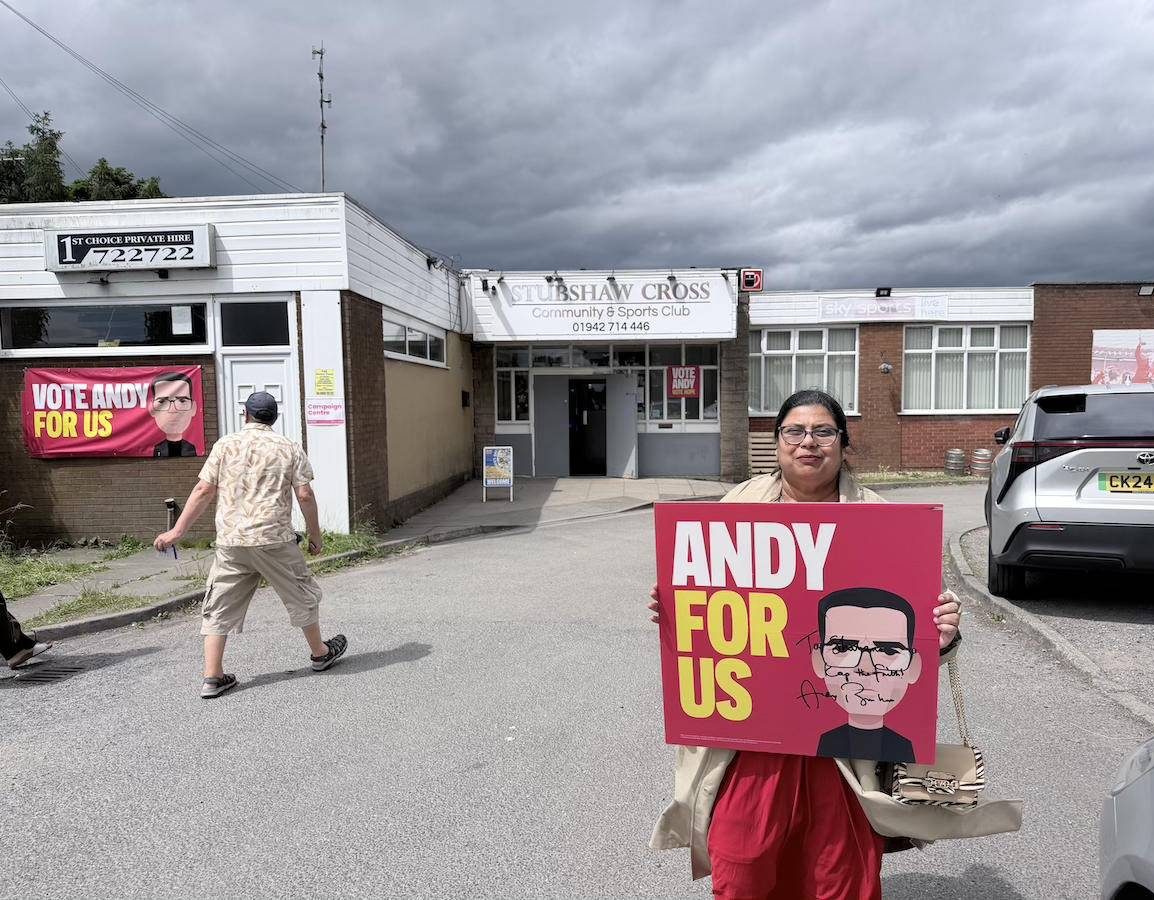 A lady holds a 'Andy For Us' placard outside of a polling station