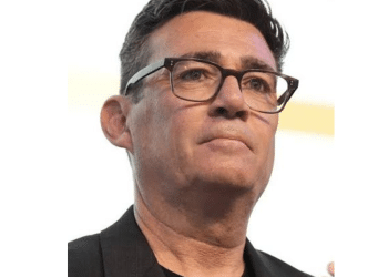 Head shot of Andy Burnham, wearing thick rimmed glasses, a crew neck tshirt and a blazer on top looking in the distance with quiet confidence. However, he has ruffled Scottish feathers.