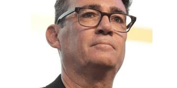 Head shot of Andy Burnham, wearing thick rimmed glasses, a crew neck tshirt and a blazer on top looking in the distance with quiet confidence. However, he has ruffled Scottish feathers.