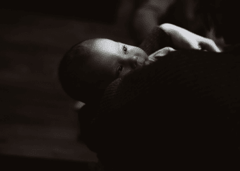 A black and white image of a newborn on someone's shoulder