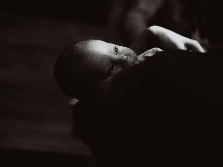A black and white image of a newborn on someone's shoulder