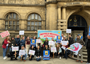 City of Sanctuary Sheffield supporters with their colourful 'Refugees Welcome Here'-type banners standing infront of what looks like a council building/ town hall