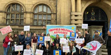 City of Sanctuary Sheffield supporters with their colourful 'Refugees Welcome Here'-type banners standing infront of what looks like a council building/ town hall