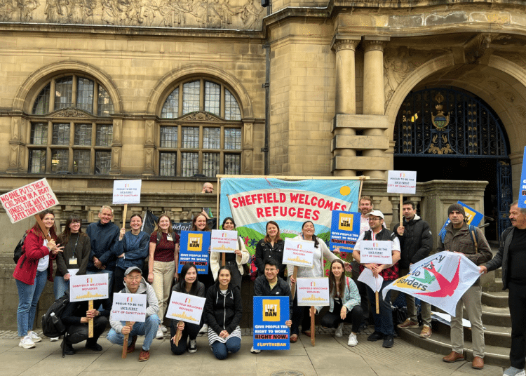 City of Sanctuary Sheffield supporters with their colourful 'Refugees Welcome Here'-type banners standing infront of what looks like a council building/ town hall