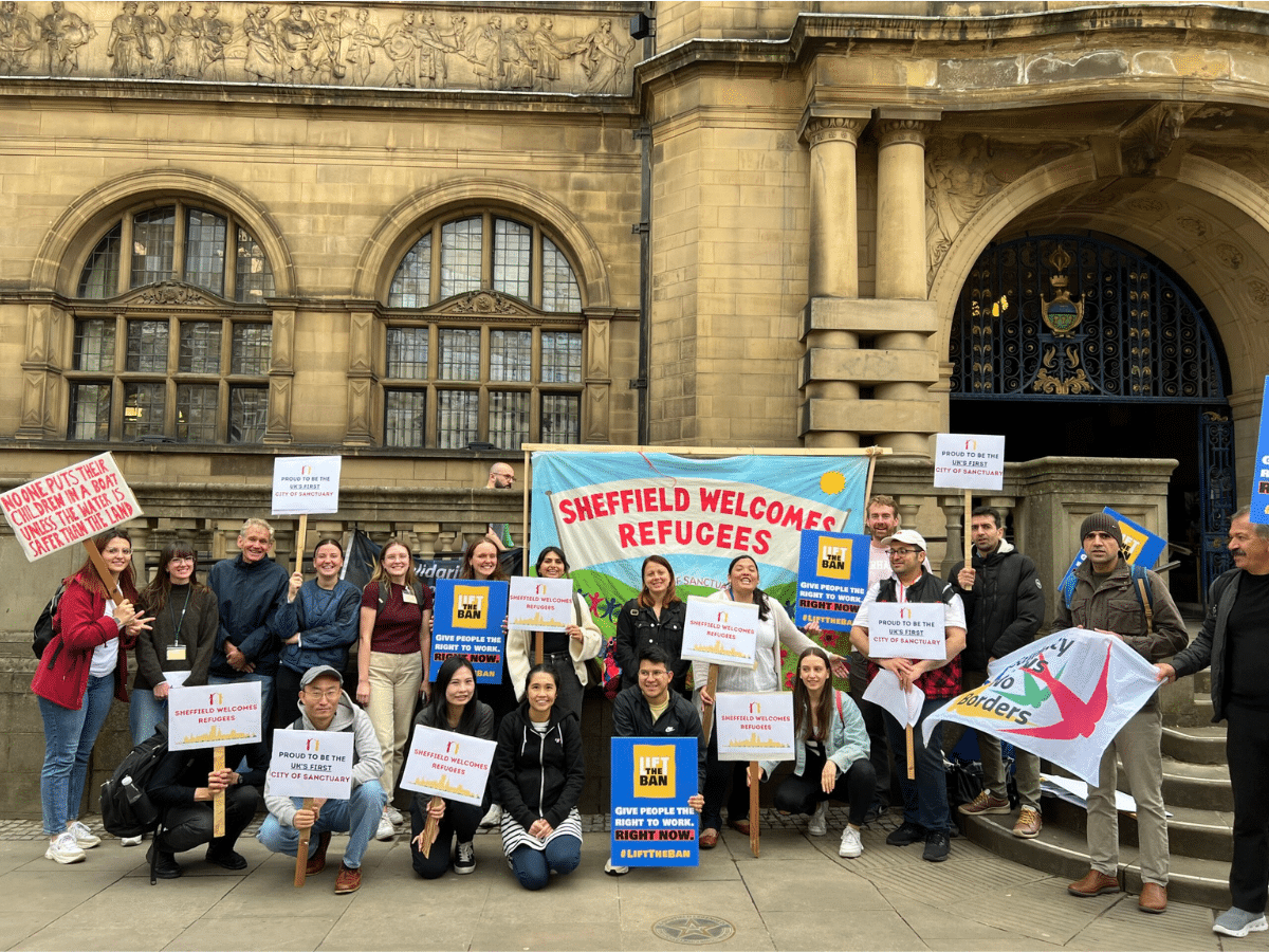 City of Sanctuary Sheffield supporters with their colourful 'Refugees Welcome Here'-type banners standing infront of what looks like a council building/ town hall