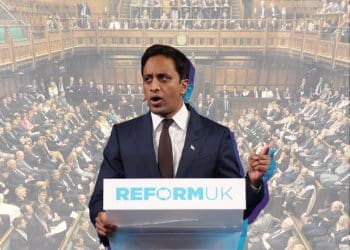 Zia Yusuf at a Reform-branded podium speaking with an image of a packed House of Commons behind him