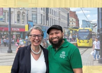 Geraldine Coggins and Mothin Ali of the Green Party smile next to one another in front of an image of a Manchester high street