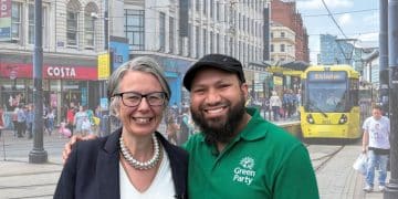 Geraldine Coggins and Mothin Ali of the Green Party smile next to one another in front of an image of a Manchester high street