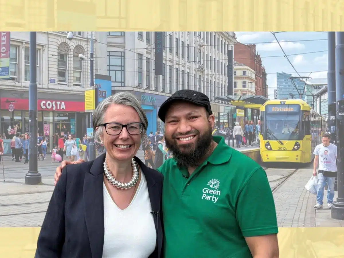 Geraldine Coggins and Mothin Ali of the Green Party smile next to one another in front of an image of a Manchester high street