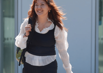Ellie Kamio, one of the Filton 25, smiling while walking outside Woolwich Crown Court, London, in April 2026 with one hand on her shoulder keeping her backpack strap in place