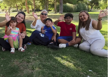 A family with young children wave and smile while sat on grass as part of a news report on Spain's approach to immigration in October 2025