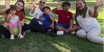 A family with young children wave and smile while sat on grass as part of a news report on Spain's approach to immigration in October 2025