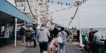 A bustling scene at Llandudno promenade in Wales with people walking near a Ferris wheel adorned with flags. Days out like this will not be affordable for many UK families due to money worries.
