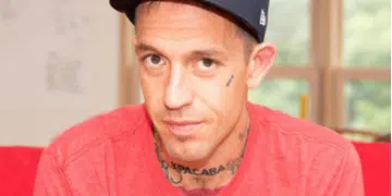 Fergie Chambers, who has small face tattoos and a neck tattoo on show above his crew neck tshirt, looks at the camera from beneath his baseball cap. He is a vocal supporter of Palestine.