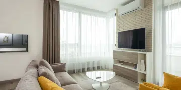 A modern living room, immaculately furnished, with an air conditioning unit on the wall above the TV. Hot weather will make more residents consider installing these.