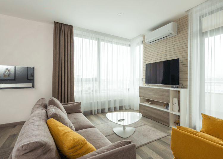 A modern living room, immaculately furnished, with an air conditioning unit on the wall above the TV. Hot weather will make more residents consider installing these.