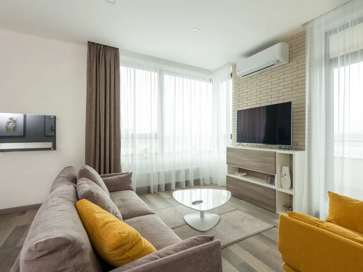 A modern living room, immaculately furnished, with an air conditioning unit on the wall above the TV. Hot weather will make more residents consider installing these.
